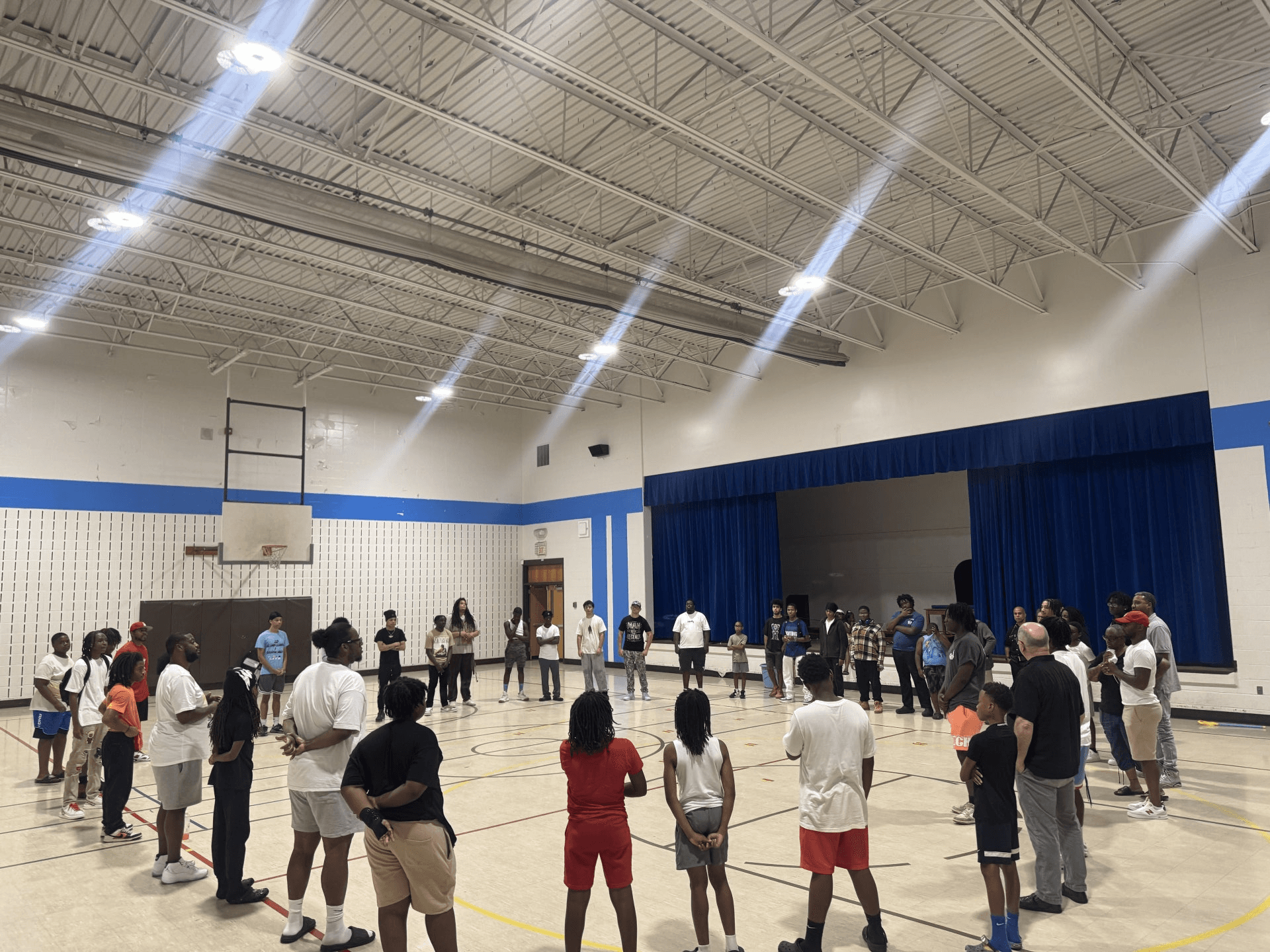 Youth and mentors stand in a large circle in a school gym during Leaders Circle